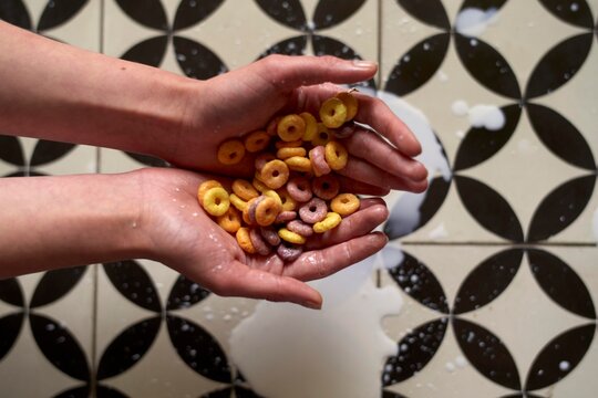 Hands Holding Colorful Cereal Spilled Over Patterned Floor Tiles