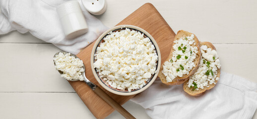 Bowl with fresh cottage cheese and bread slices on white wooden background