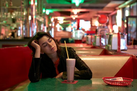 Woman sitting alone in a retro diner with milkshake 