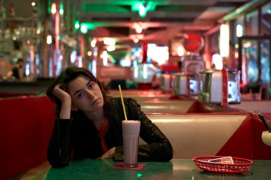 Young woman sitting alone in diner deep in thought 