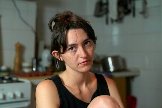 Young Woman Sitting in Kitchen With Serious Expression