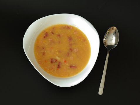 Delicious and nutritious pea soup with smoked meats and a tablespoon on a black background.