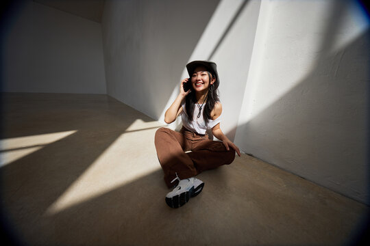 Young woman in stylish outfit smiling while talking on phone ind