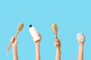 Female hands with bottle of cosmetic product, massage brushes and bath sponge on blue background