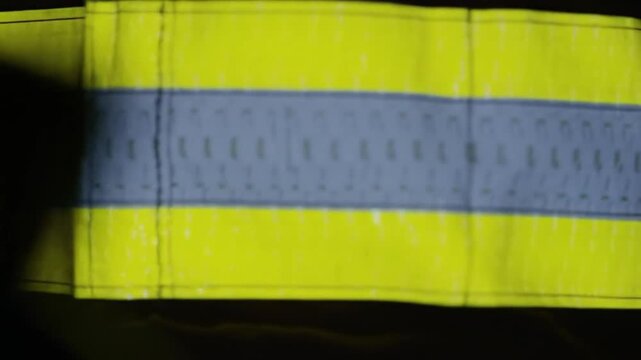 Detail of a bright yellow high-visibility safety vest with a gray retroreflective stripe for worker protection.