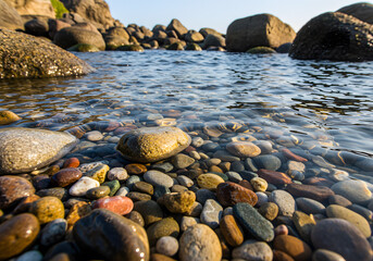 Fototapeta premium Calm Coastal Scene Pebbles, Rocks, and Clear Water Under Blue Sky - Natural Landscape Photography