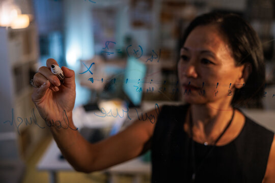 Woman writes equations on glass board