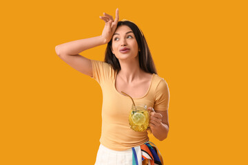 Beautiful young tired woman with mason jar of infused lemon water on yellow background