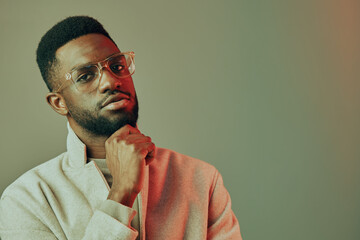 Thoughtful young African man wearing glasses in a stylish gray jacket, posing confidently against a soft pastel background, perfect for personal branding and lifestyle imagery