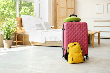 Suitcase with neck pillow and backpack on floor in hotel room interior
