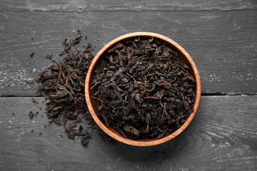 Bowl with dry black tea leaves on black wooden background