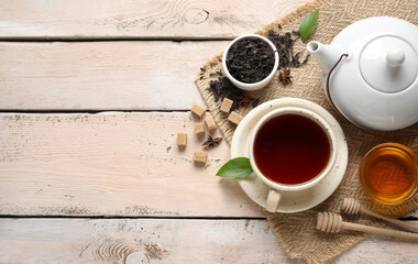 Cup of hot black tea and bowl with dry leaves on white wooden background