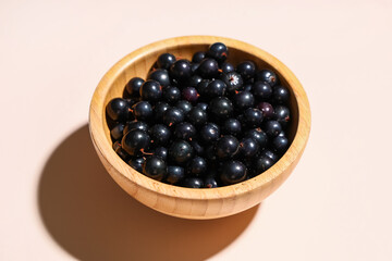 Wooden bowl with fresh black currants on beige background