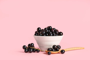 Bowl and wooden spoon with fresh black currants on pink background