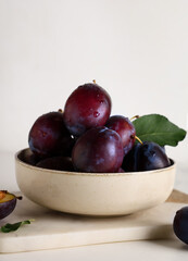 Bowl with fresh ripe plums on white background
