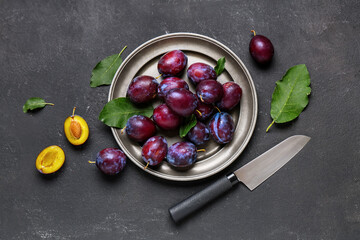 Plate with fresh ripe plums on black background
