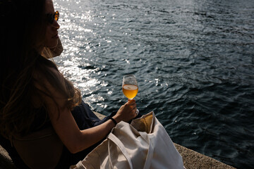 Woman’s silhouette holding a glass of orange wine next to a river
