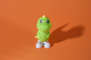 Front View of a Cute Green Toy Dinosaur on an Orange Background