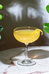 Yellow cocktail drink with whiskey, liqueur and lemon juice. Marble table in elegant bar with tropical leaves
