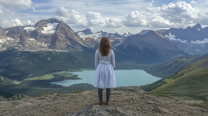 Naklejka premium Woman in white dress standing on mountain peak overlooking alpine lake