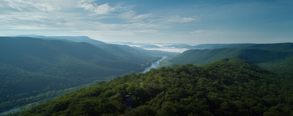 Fototapeta premium Verdant mountains roll toward the horizon under a partly cloudy blue sky, a river flows through
