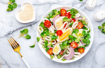 Gourmet seafood salad with squid, juicy orange, red tomatoes, lamb lettuce on marble table, top view