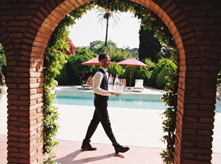 Waiter carrying tray with drinks by the poolside at a luxury resort