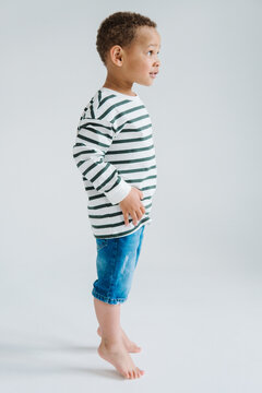Young child in striped shirt and jeans stands barefoot in studio