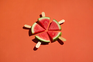 Watermelon slices on popsicle sticks create a vibrant orange