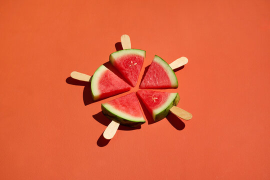 Watermelon slices on popsicle sticks create a vibrant orange