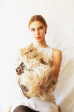 Fashion-forward portrait of blonde model with pet cat &ndash; clean backdrop
