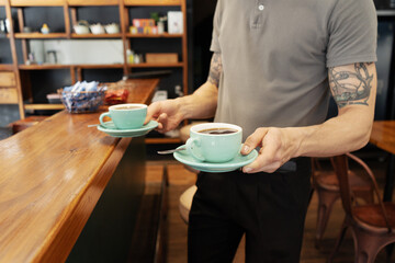 Hands of barista serving coffee to customers at table