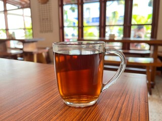 Glass Cup of Hot Black Tea on Wooden Table in Cozy Café