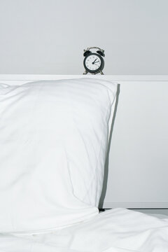 Classic Black Alarm Clock on a Bedside Shelf next to a White Pillow