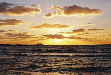 Golden sunset over the ocean with dramatic clouds and film grain texture