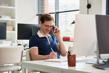 Man Working at Desk Talking on Phone in Bright Office Setting