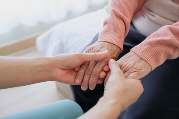 A woman holds hands and gives love to her elderly mother at home, creating bonding and happiness. love and care concept