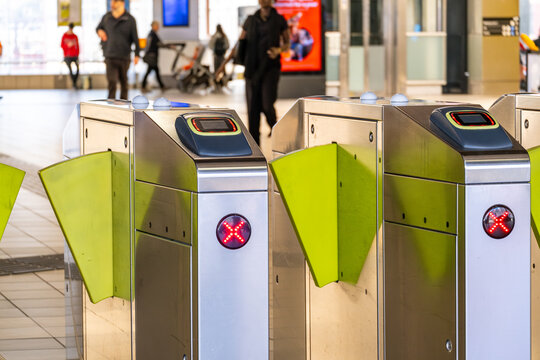 Automatic ticket barriers with red &lsquo;X&rsquo; lights at a train station in Melbourne, Australia, indicating closed gates, with commuters walking in the background at a railway station.