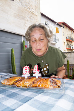 Senior woman blowing out candles on 64th birthday cake