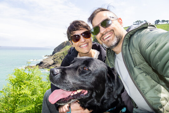 Couple taking selfie with dog by the sea during hiking trip