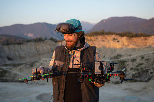 Drone pilot holding two FPV quads at sunset