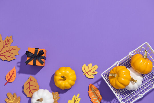 Basket filled with pumpkins and leaves on purple backdrop