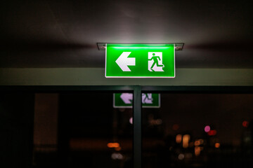 Illuminated exit sign points left, with city lights beyond.