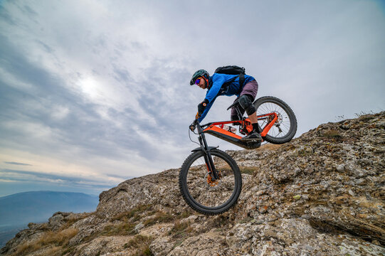 Mountain biker descends rocky cliff at sunset