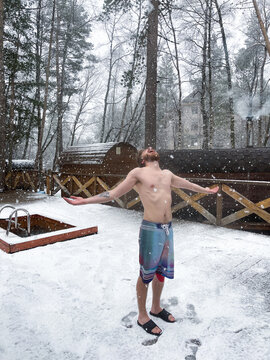 Shirtless man enjoying snow near winter sauna