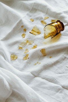Glass Jar Shattered on White Fabric Creating a Scattered Mess