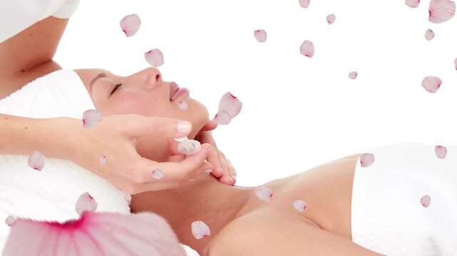 Therapist grabbing facial roller and rolling client jawline upward for spa calm while petals drift