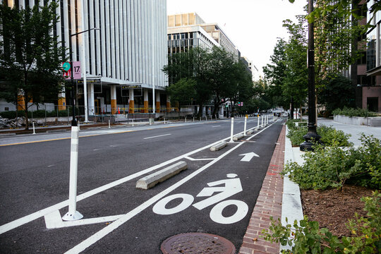 Protected urban bike lane along city street with bollards and cycling arrows. g. - Powered by Adobe