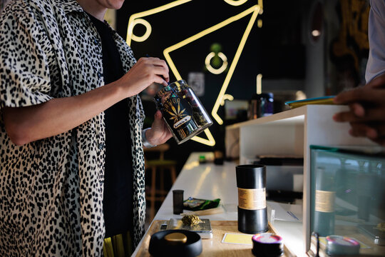 Woman preparing cannabis from labeled jar 
