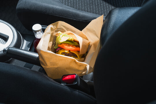 Cheeseburger in paper wrap on car console with red drink bottle